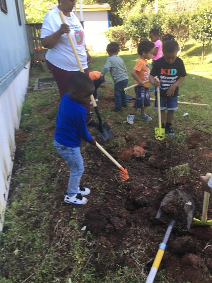 Adult and children digging in dirt with shovels and rakes