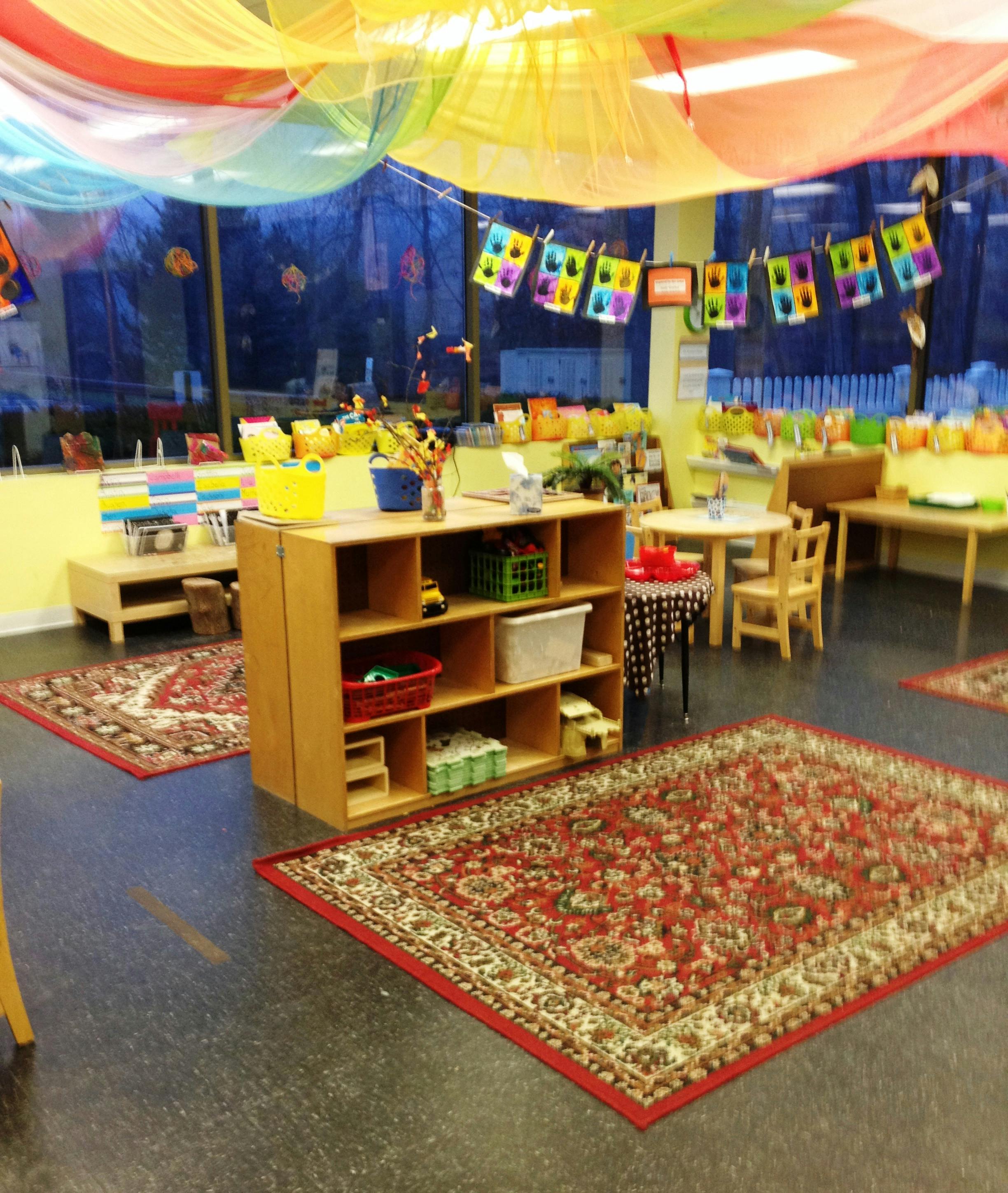 Classroom with colorful ceiling drapes, rugs, and shelves with shelves of toys