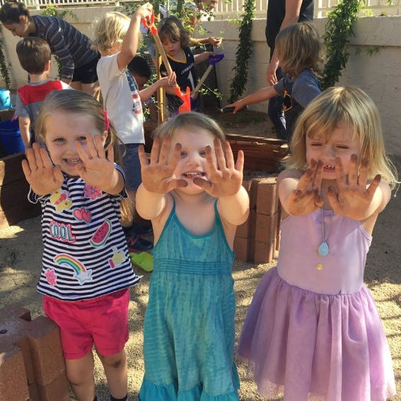 Three children with muddy hands showing their palms to the camera