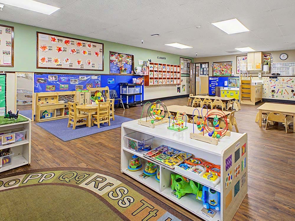 An empty classroom with small tables and chairs and toys on shelves