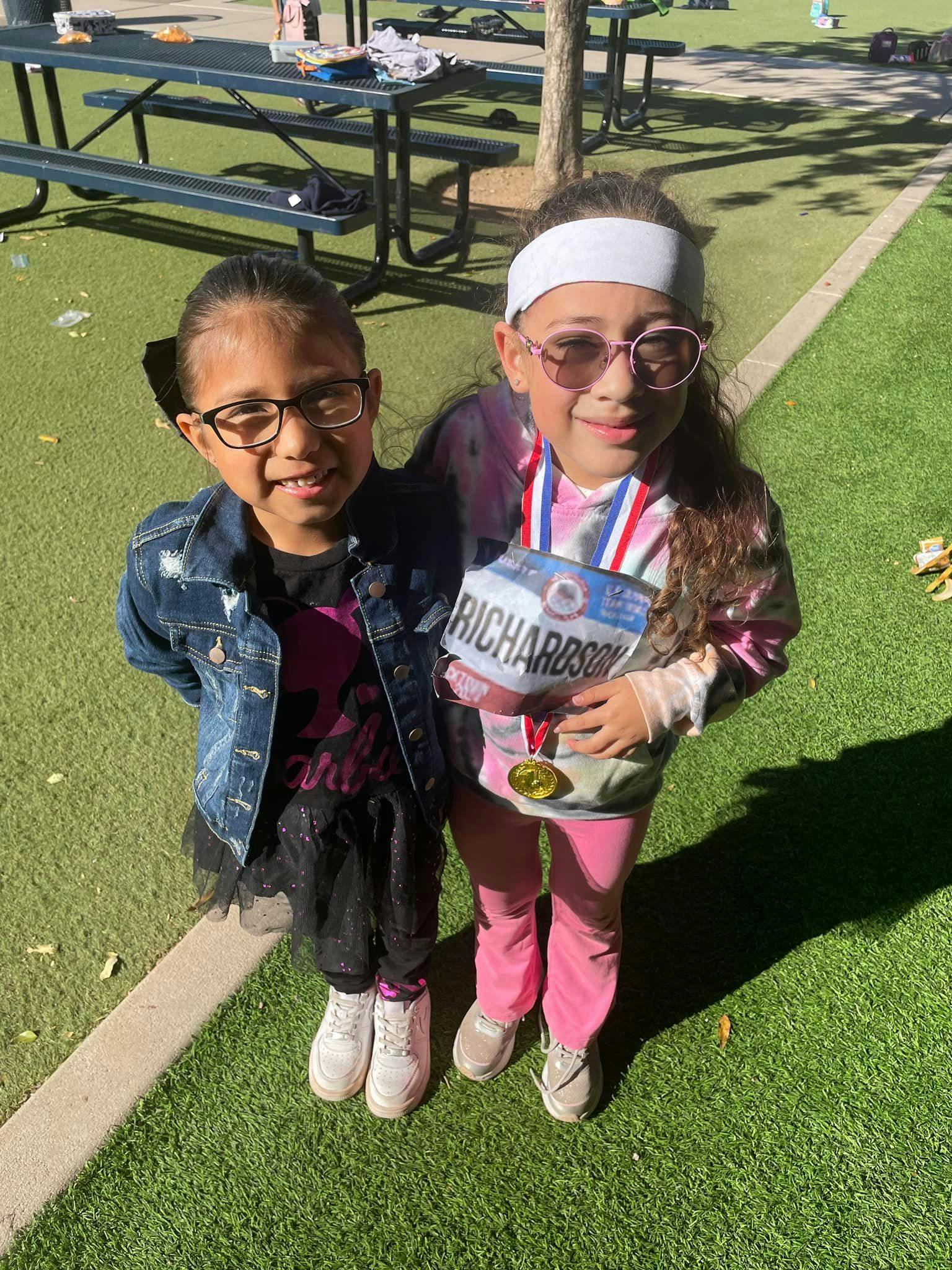 Two children standing on artificial grass, one wearing a medal and medal