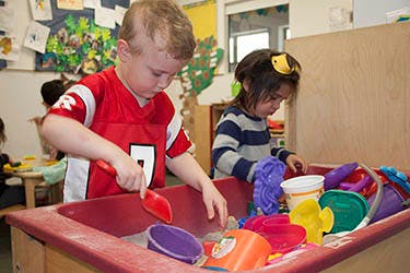 Two children playing with sand toys in a sand table
