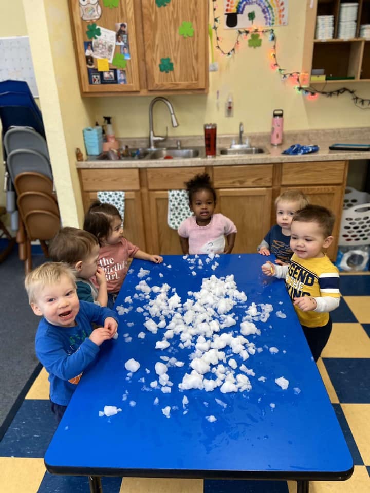 Children gathered around a blue table with white fluffy material on it