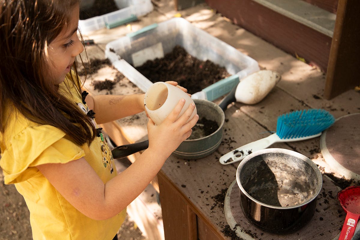 Child holding a small pot over a larger pot of dirt