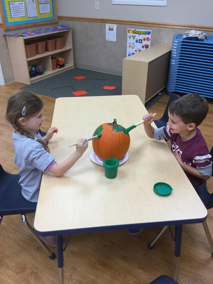 Two children painting a pumpkin in a classroom