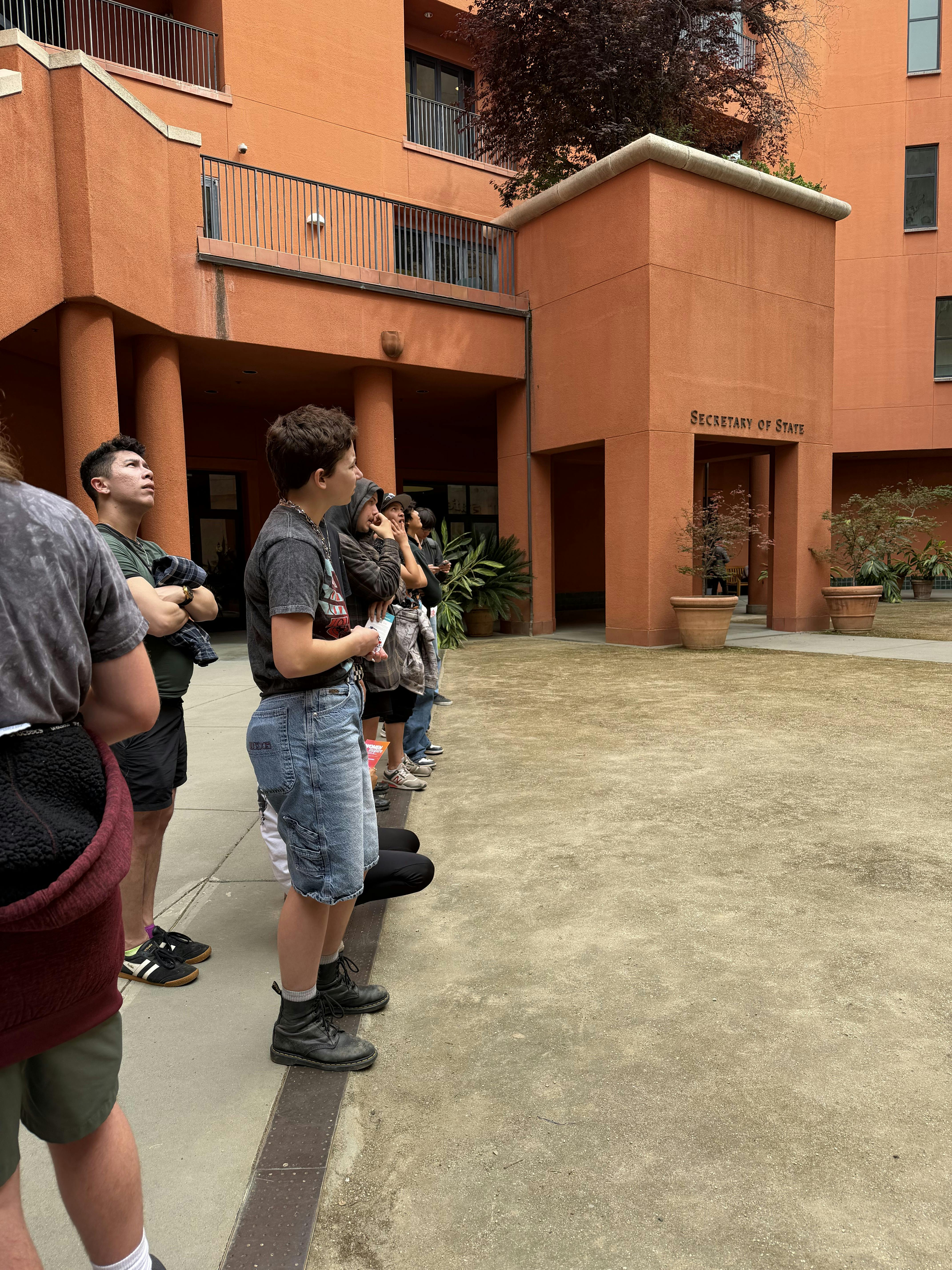 Group of people looking up at a building with text "SECRETARY OF STATE"