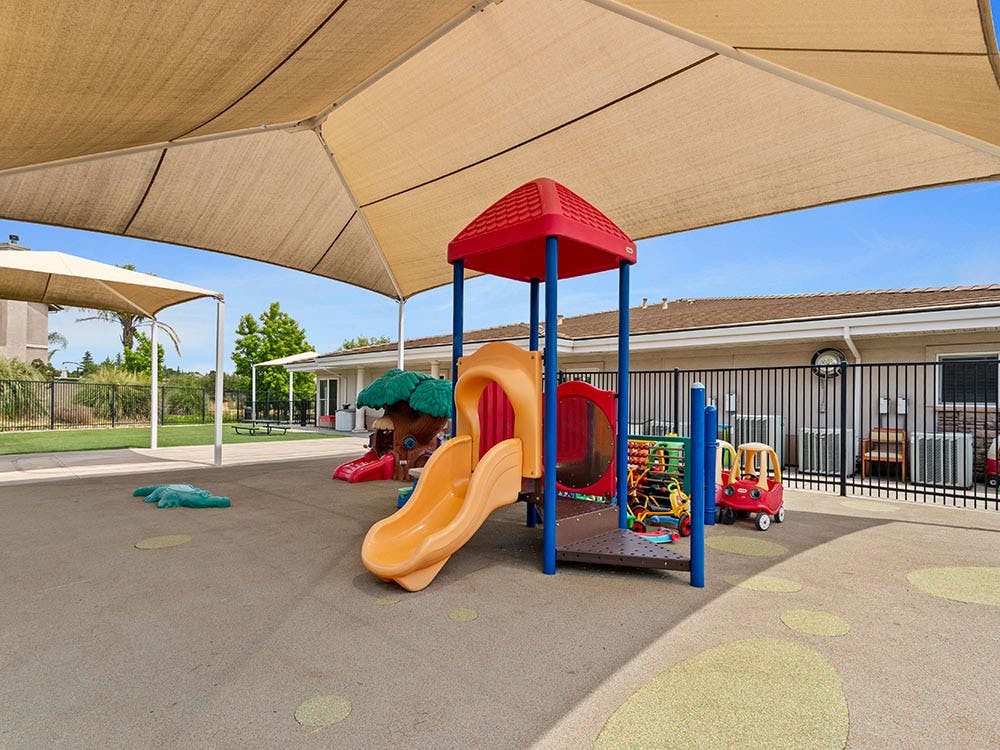 Playground with colorful play structures and a slide under a large shade canopy
