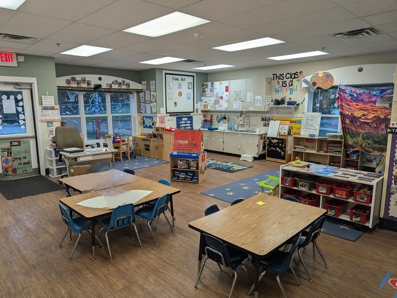 Empty classroom with small tables and chairs, exit sign above a door