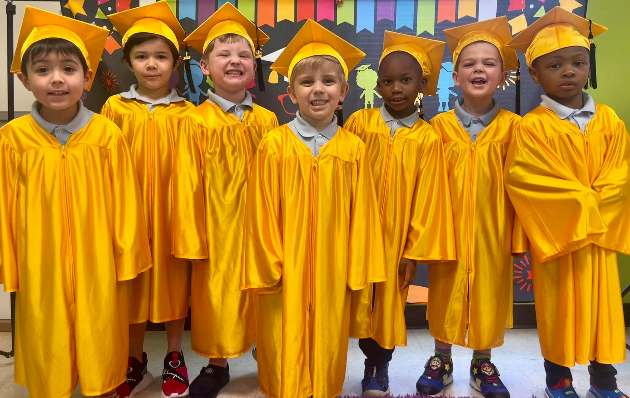 Six children in yellow graduation caps and gowns