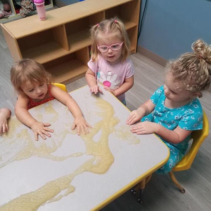 Three children playing with a liquid substance on a table