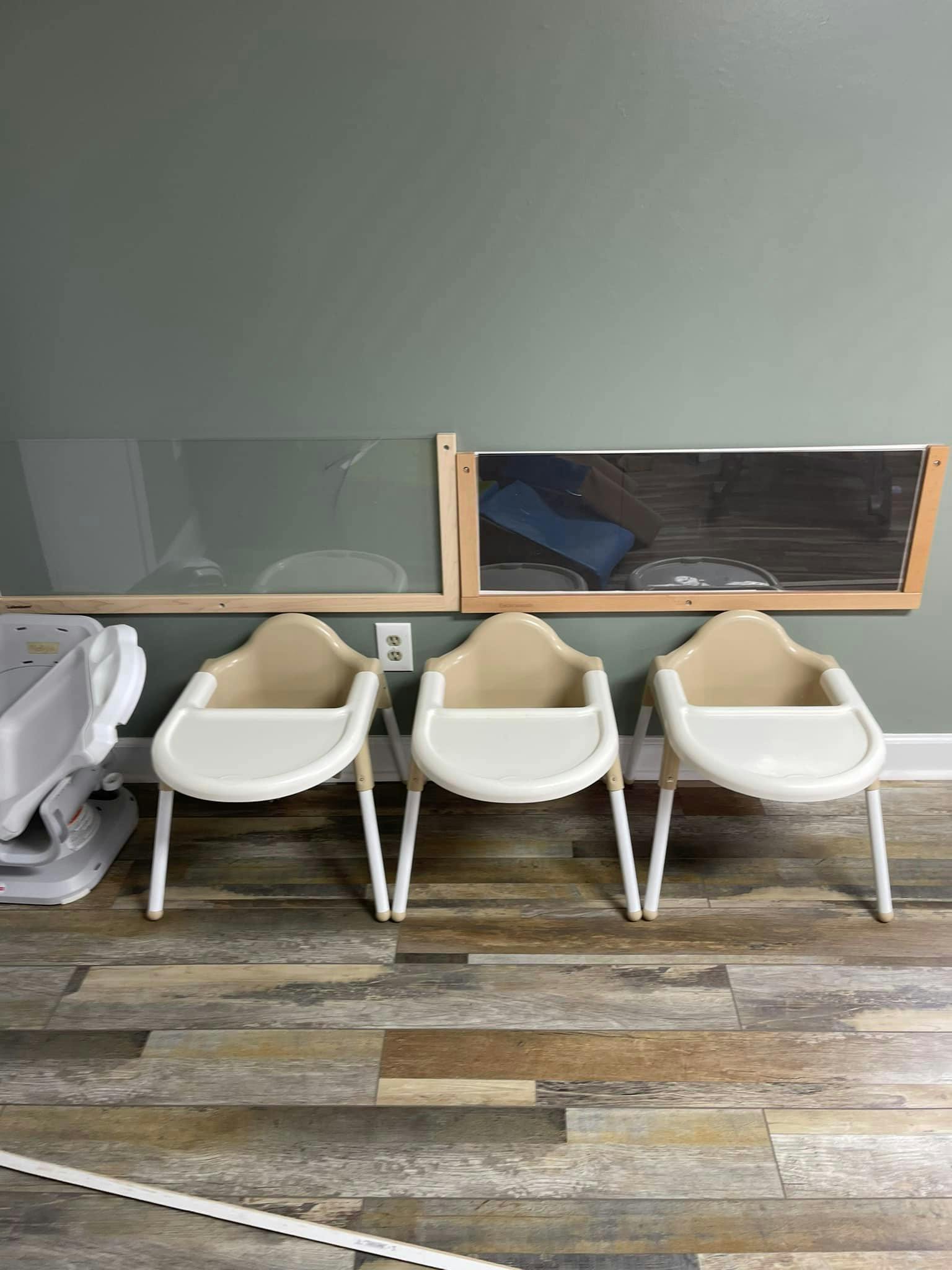 Three highchairs lined up against a wall, with a child car seat next to them
