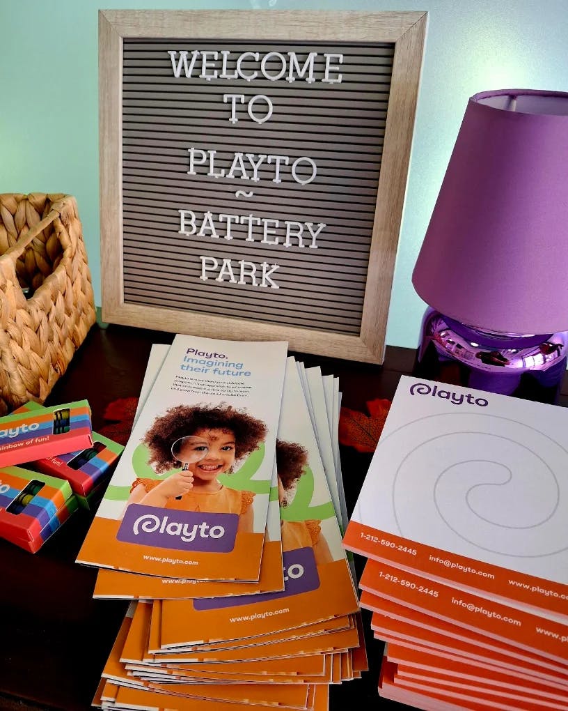 Sign reading Welcome To Playto Battery Park with stacks of informational flyers