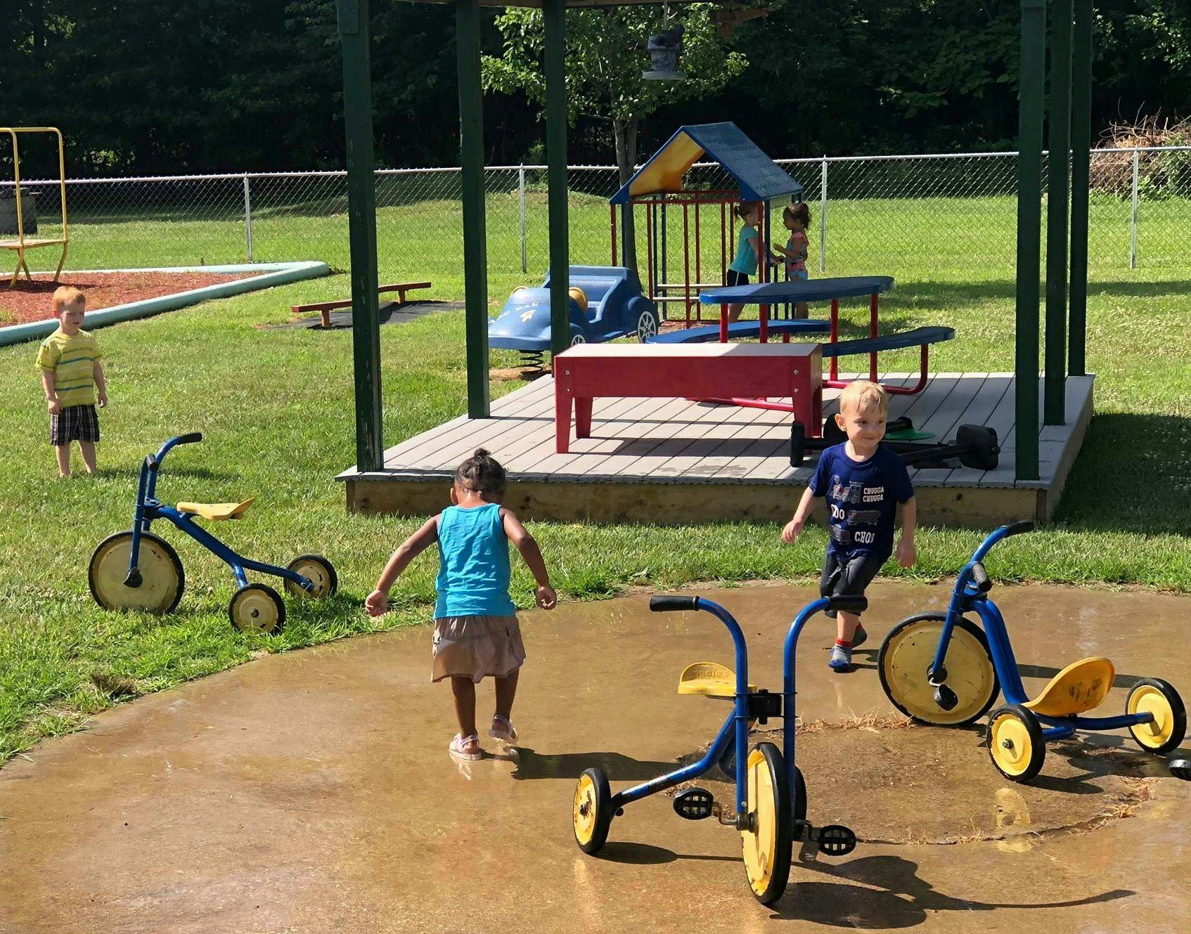 Children playing outdoors with tricycles and playground equipment