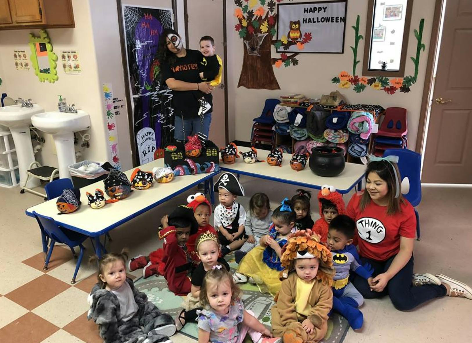 People and children in costumes in a classroom with Halloween decorations