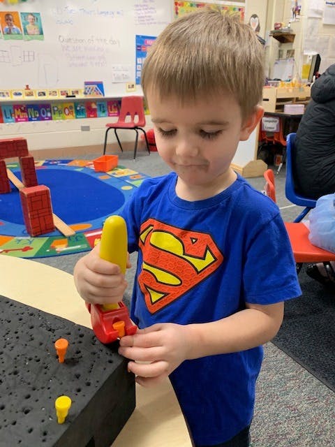 Child playing with a toy hammer and pegs in a classroom