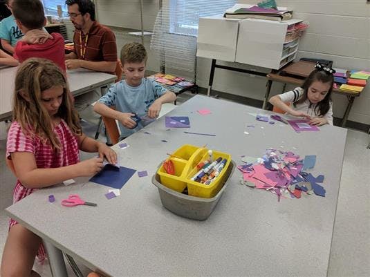 Children cutting paper at a table in a classroom