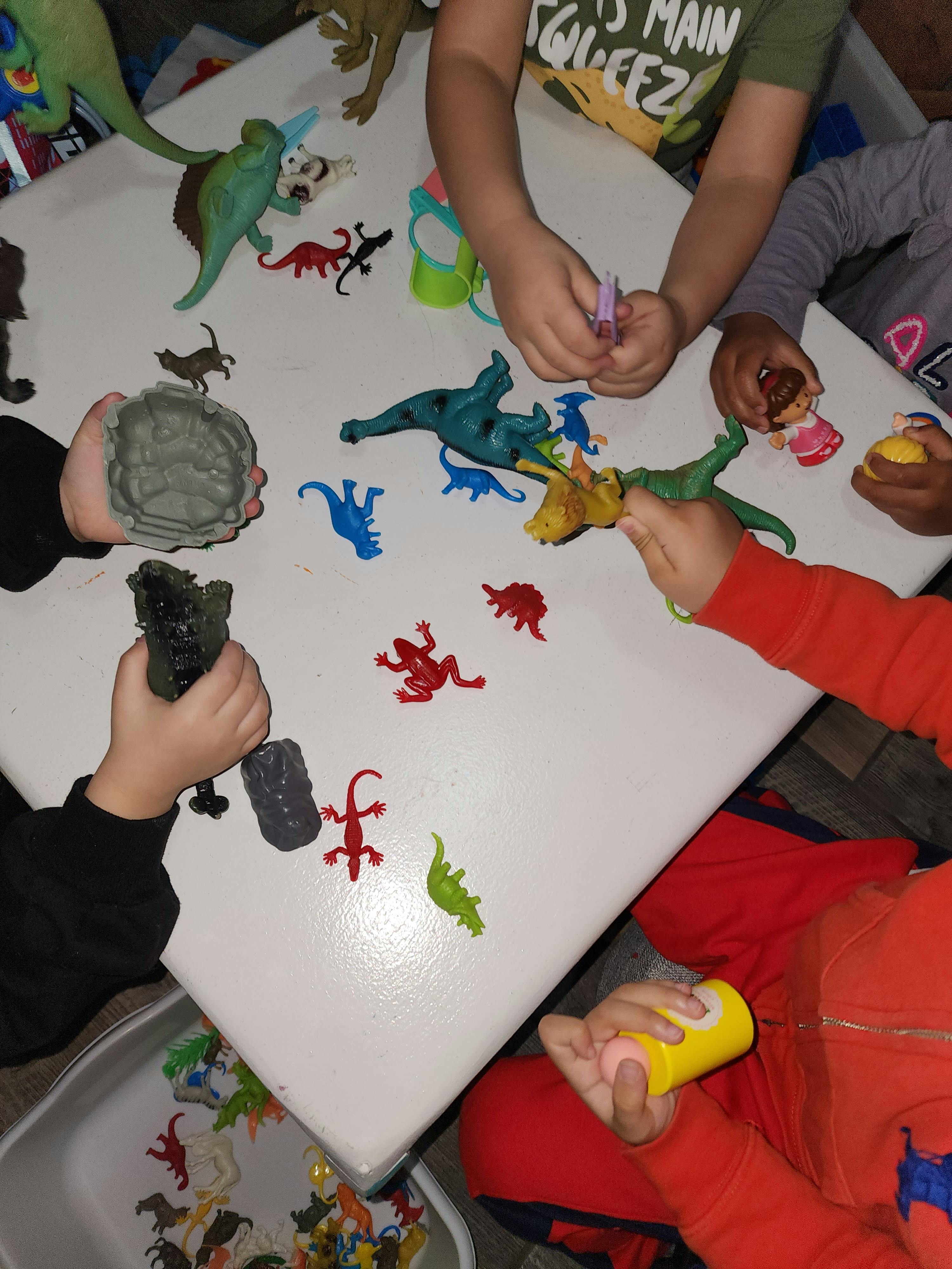 Children playing with dinosaur and lizard toys on a white table