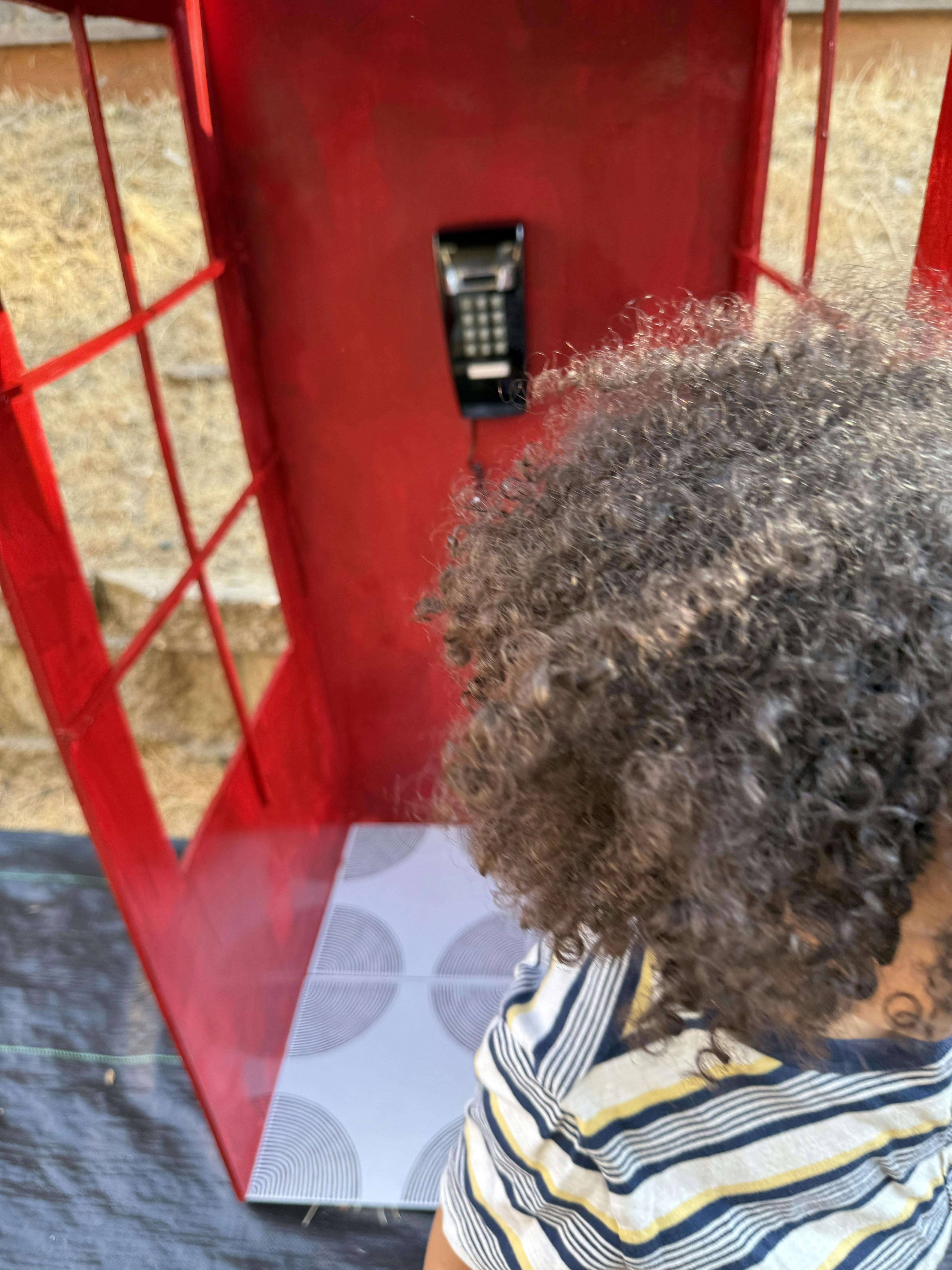 Child looking at a phone in a red phone booth