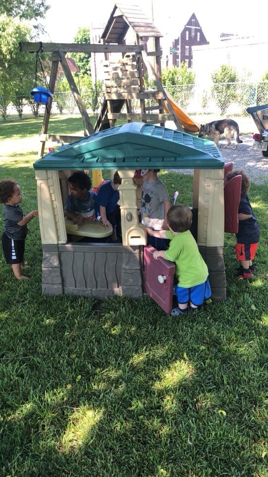 Children playing in and around a playhouse on a grassy lawn