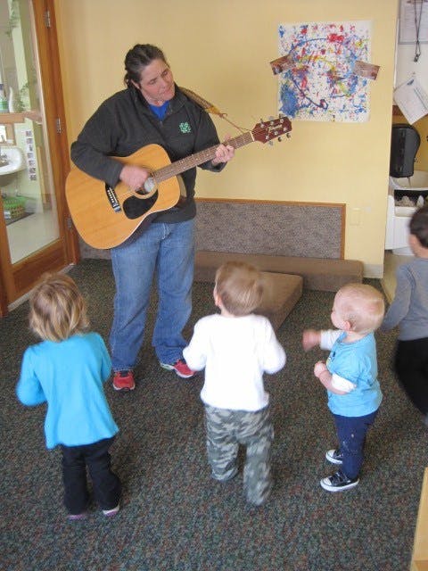 Person playing guitar for three young children in a classroom