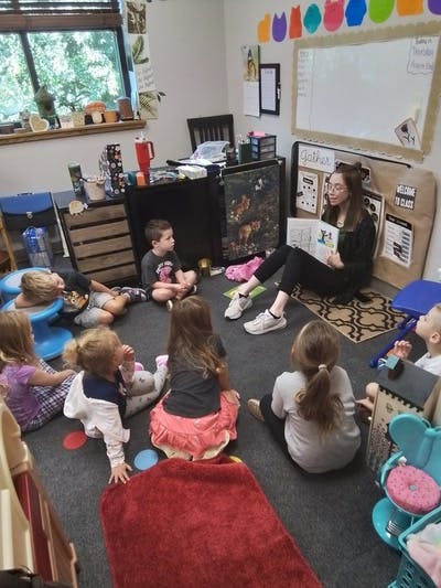 Person reading a book to a group of children in a classroom