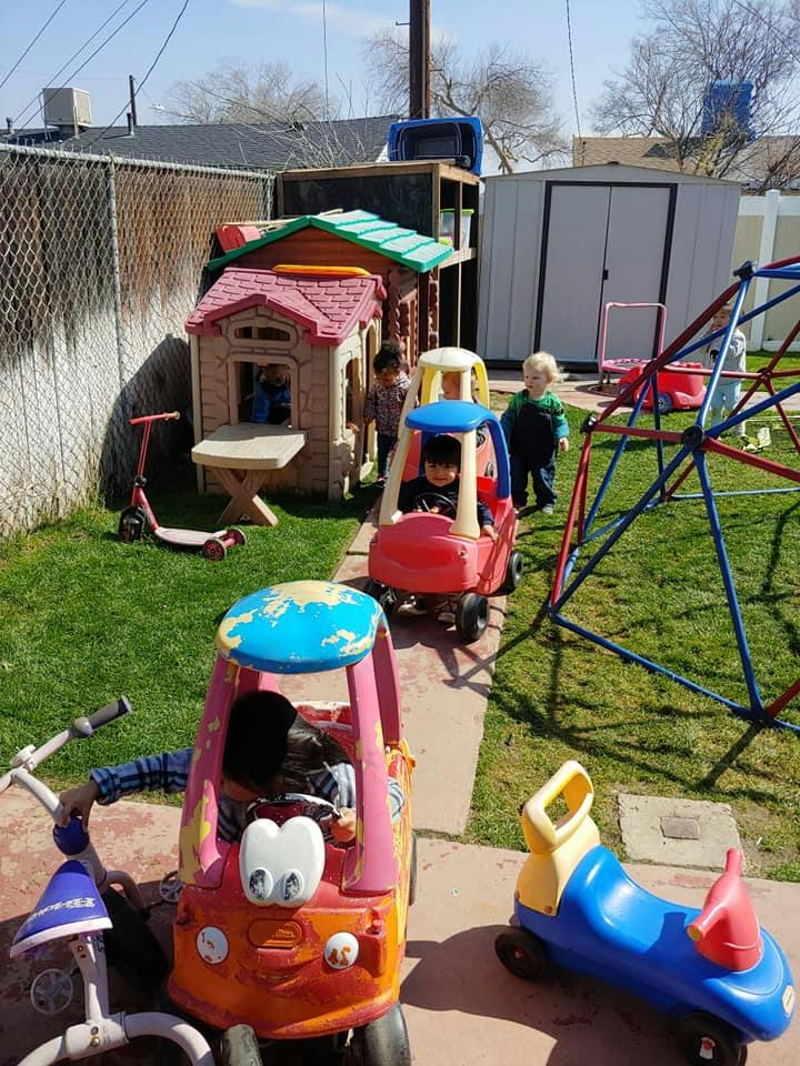 Children playing with toy cars and a playhouse in a backyard