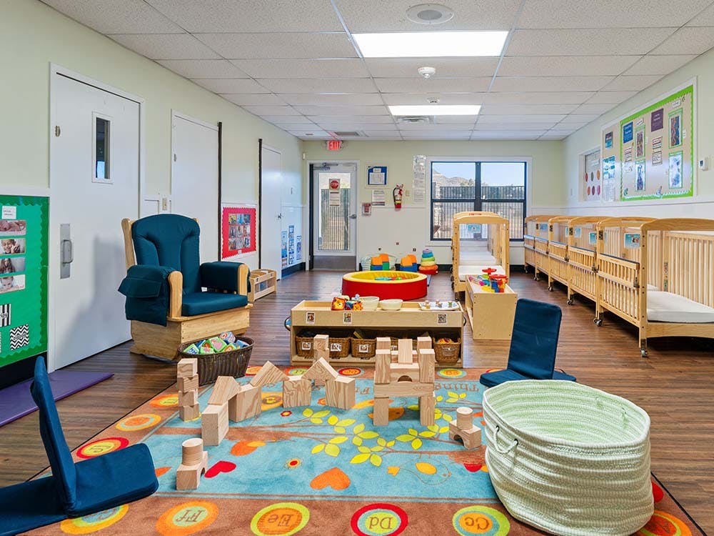 Classroom with wooden cribs, a blue rocking chair, a colorful rug, and wooden blocks
