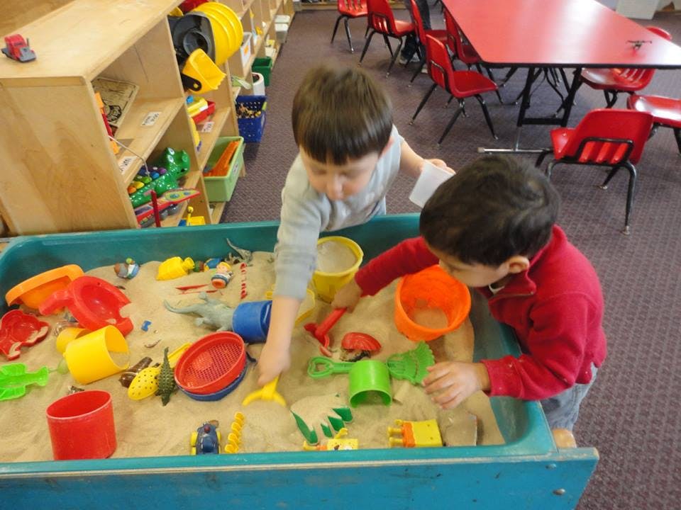 Two children playing in a sand table with toys