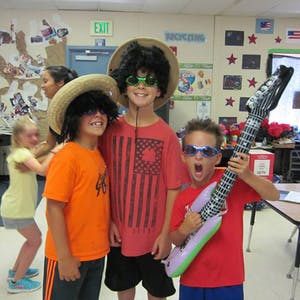 Three children in wigs and sunglasses, one holding an inflatable guitar