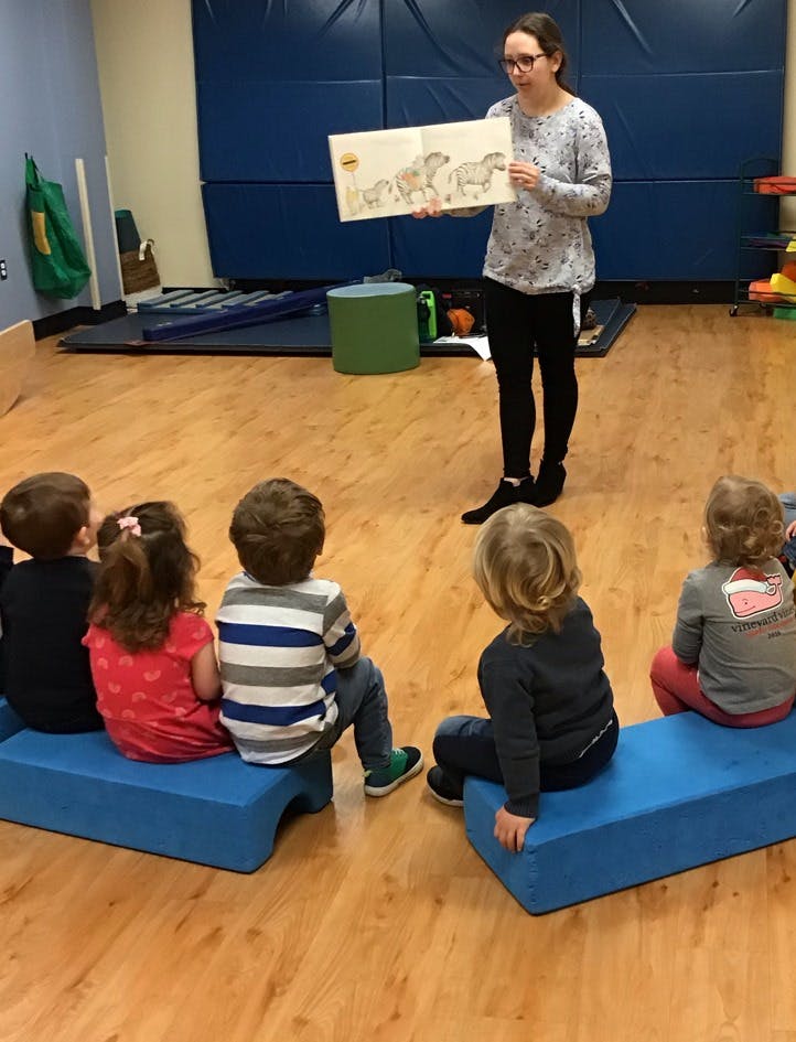 Person reading a book to a group of children sitting on blue benches