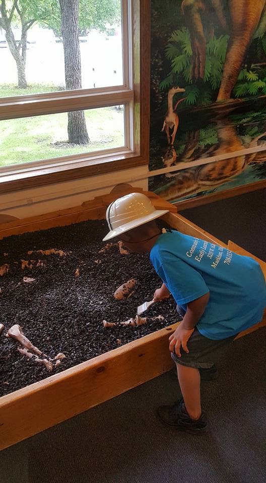 Child in a pith helmet digging in a sandbox with a small shovel