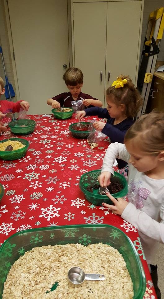 Children at a table with a red snowflake tablecloth, scooping ingredients from bowls