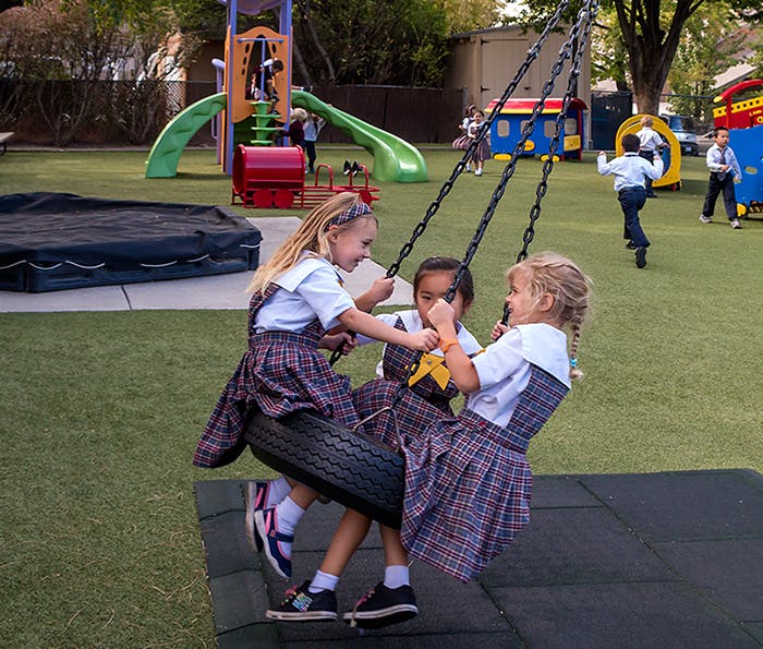 Three children in plaid uniforms sitting on a tire swing at a playground