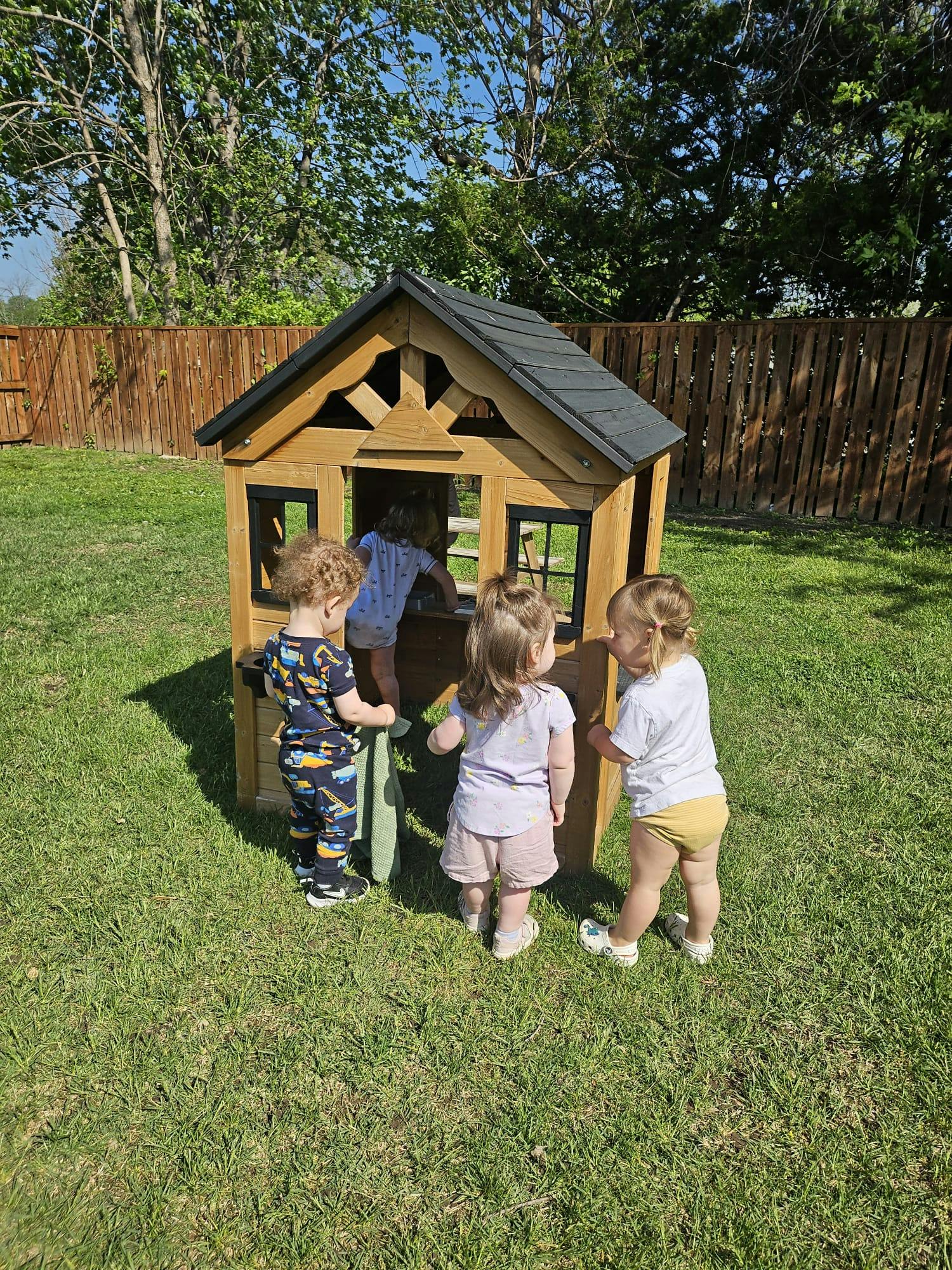 Children playing around a small wooden playhouse in a grassy yard