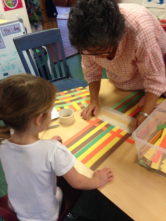 Person and child weaving paper strips together at a table