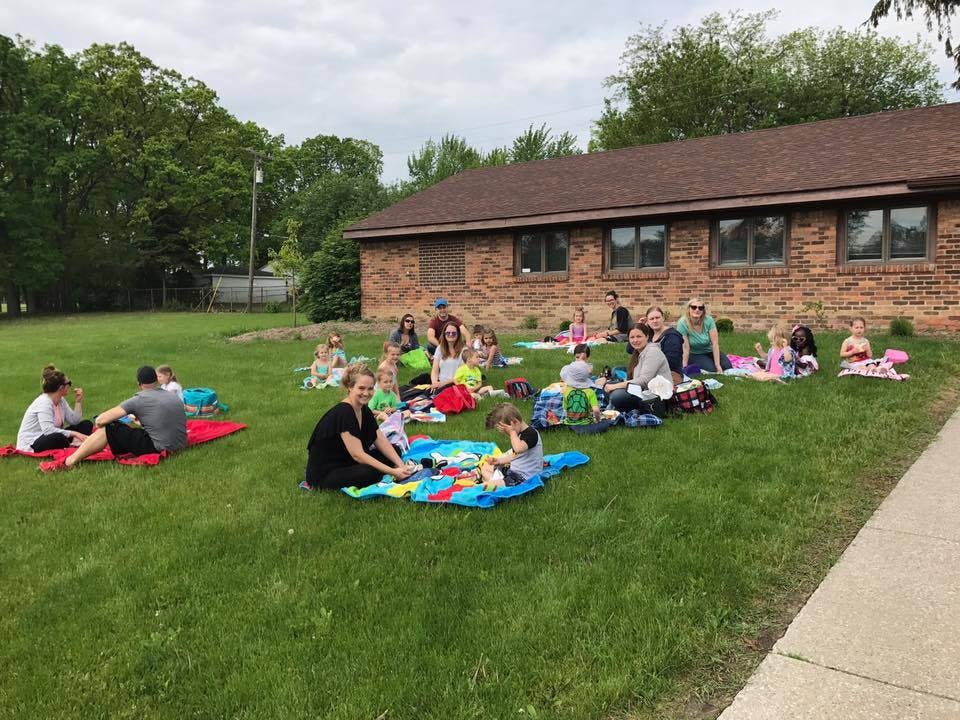People and children sitting on blankets on a grassy lawn