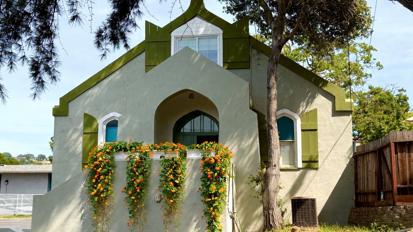 A cream-colored building with green trim and orange flowers cascading from a planter