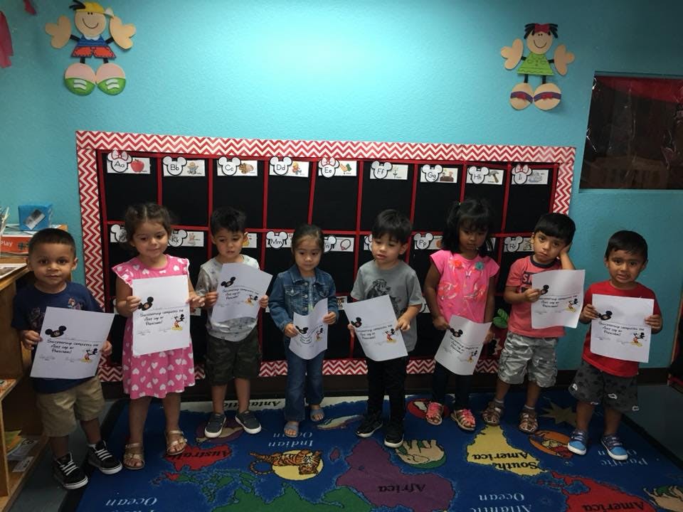 Seven children holding up papers in a classroom