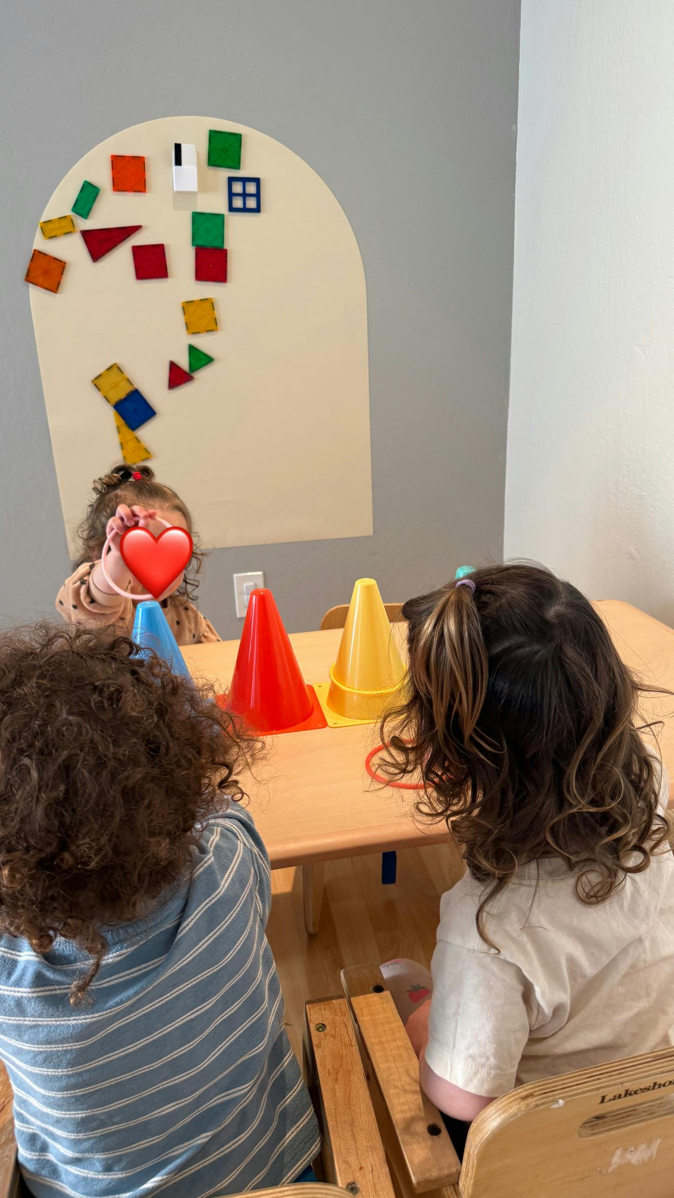 Three children playing with plastic cones and rings at a table