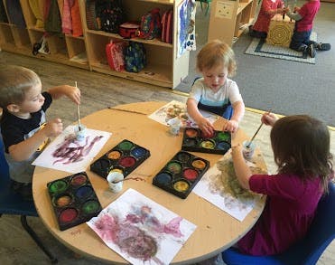 Three children painting at a round table in a classroom