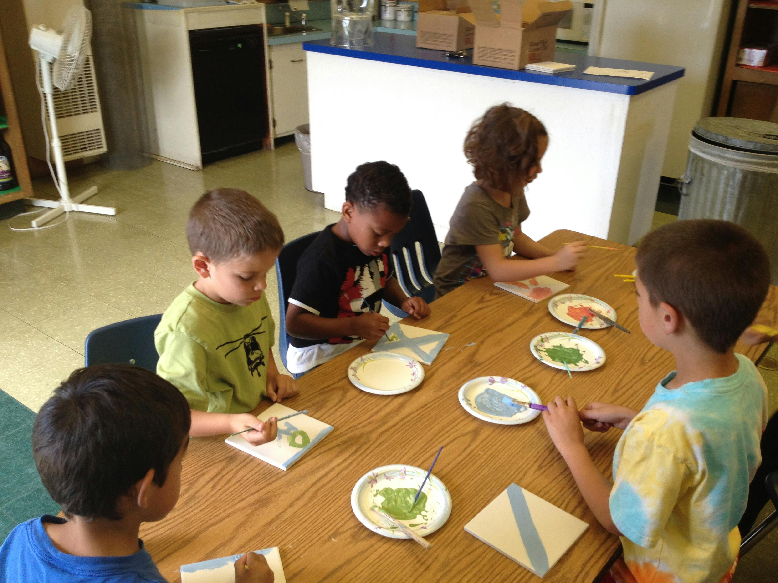 Children sitting at a table painting small plates of paint and painting small canvases