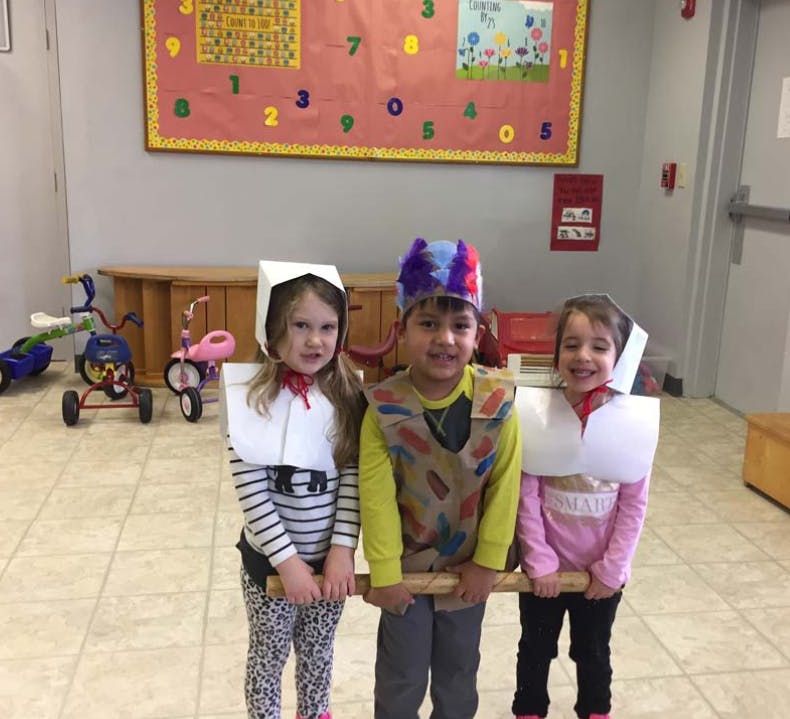 Three children in costumes holding a wooden stick in a classroom