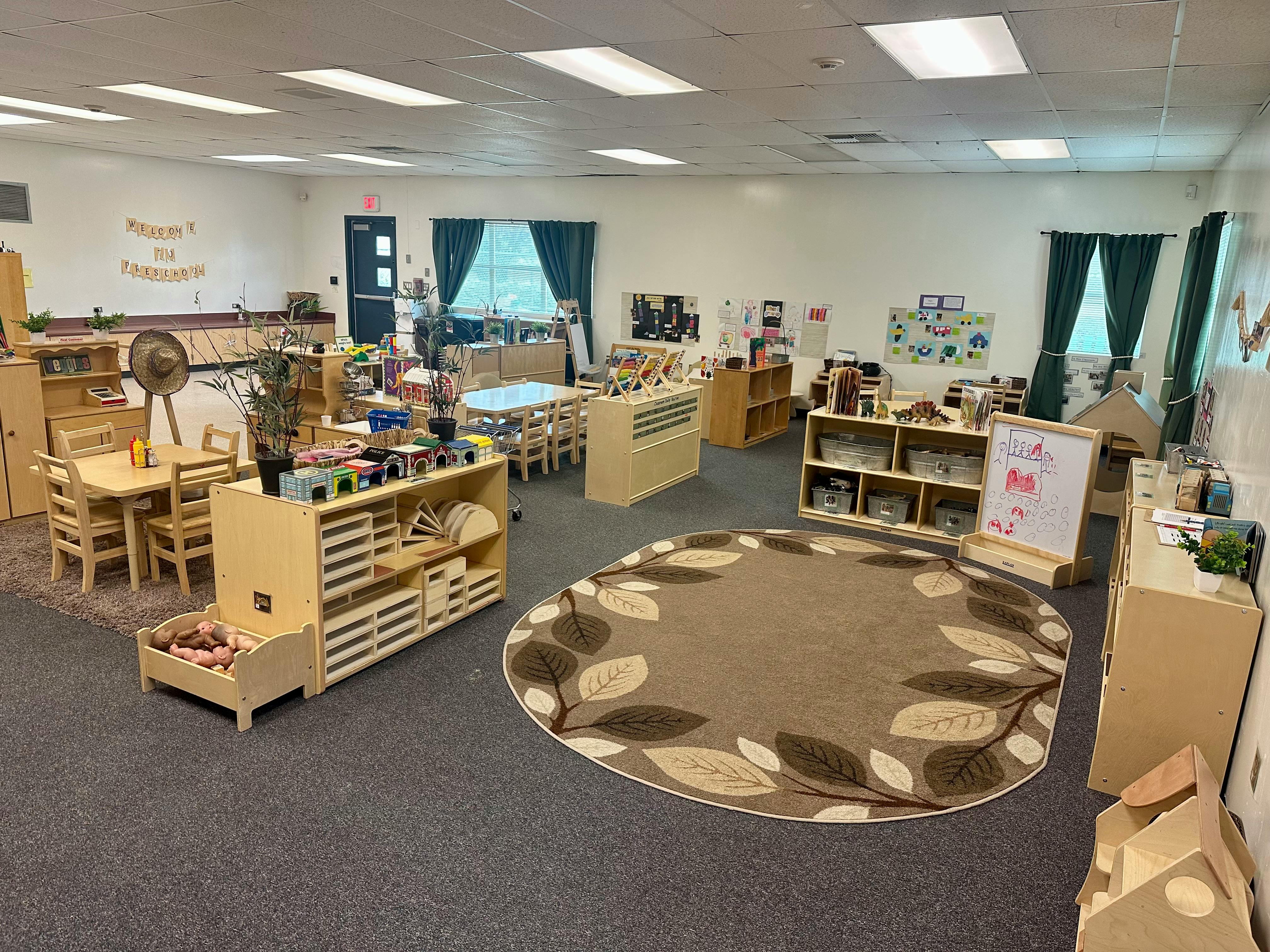 Classroom with small tables and chairs, shelves, and a round rug