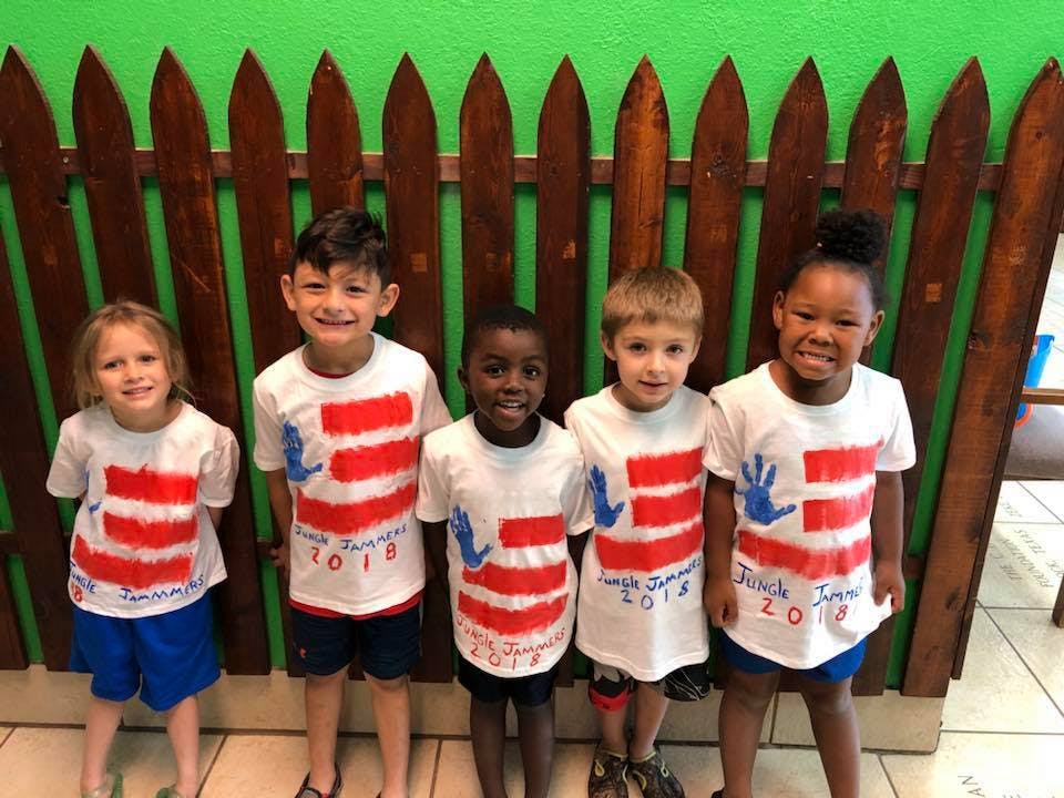 Five children in matching shirts standing in front of a fence