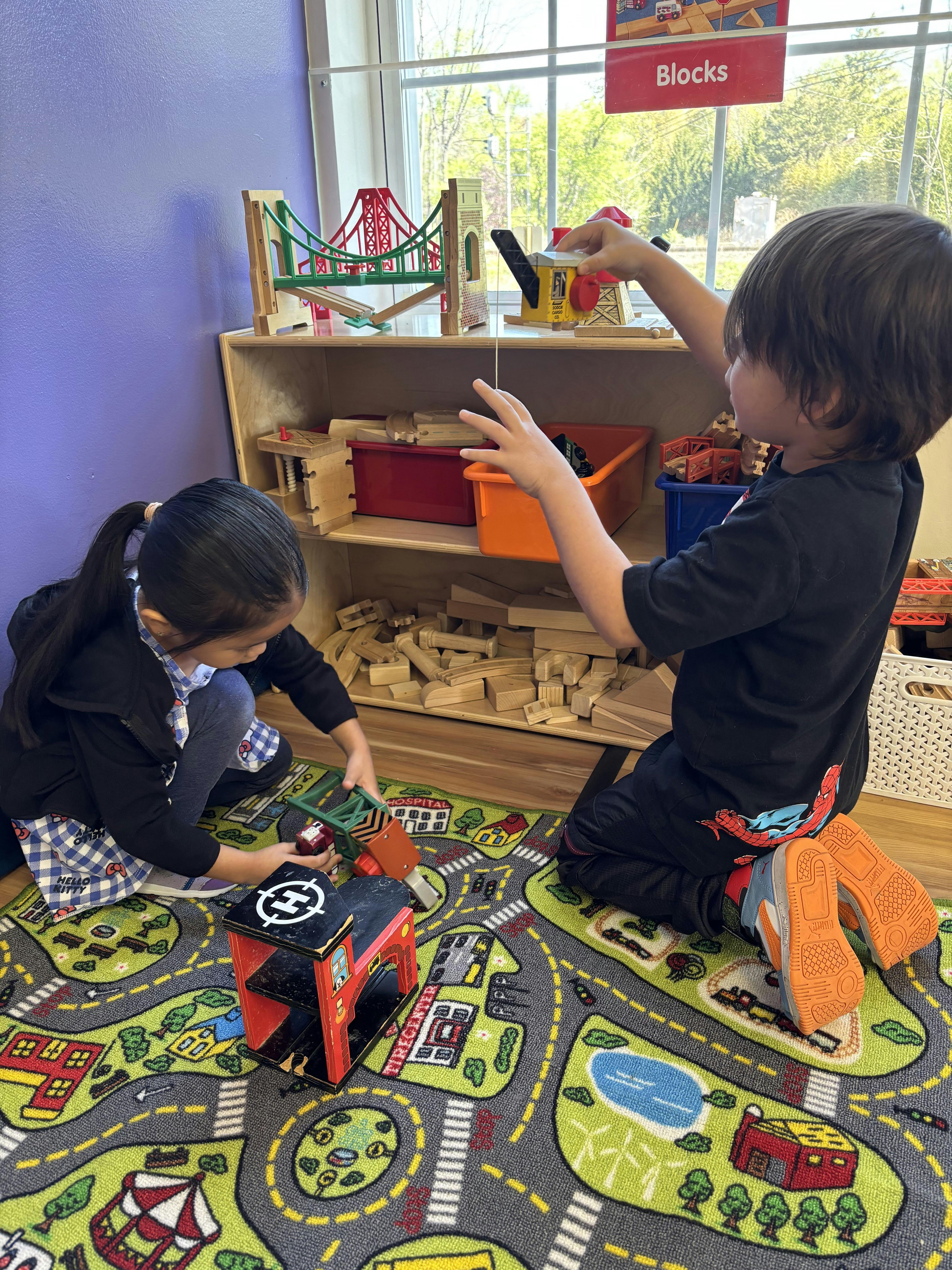 Two children playing with toy blocks and trains in a classroom