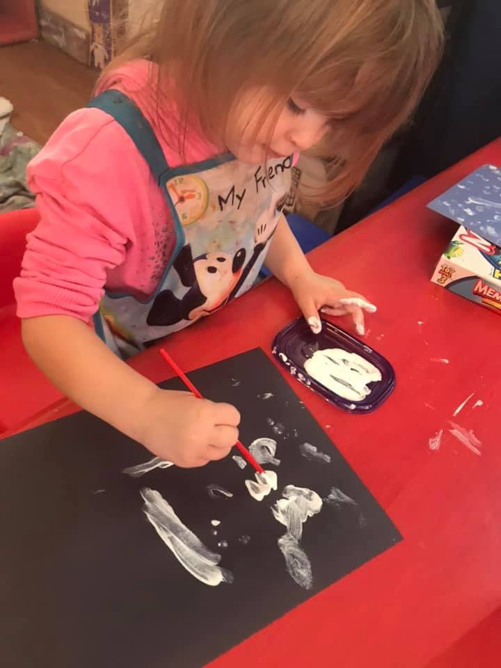 Child painting with white paint on black paper