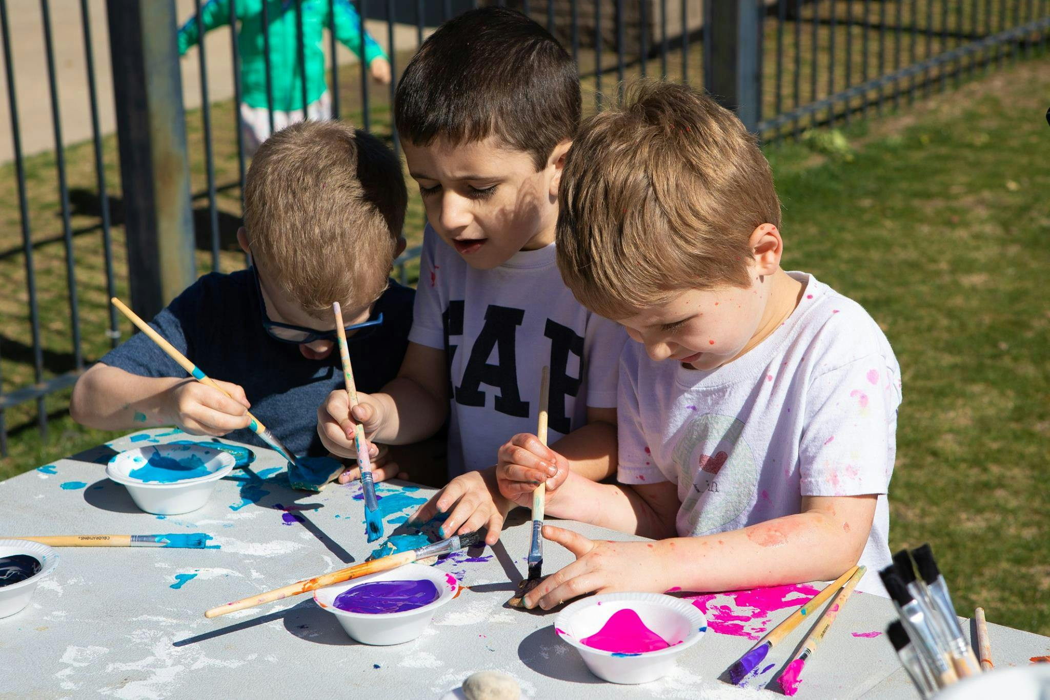 Three children painting with brushes and colorful paints
