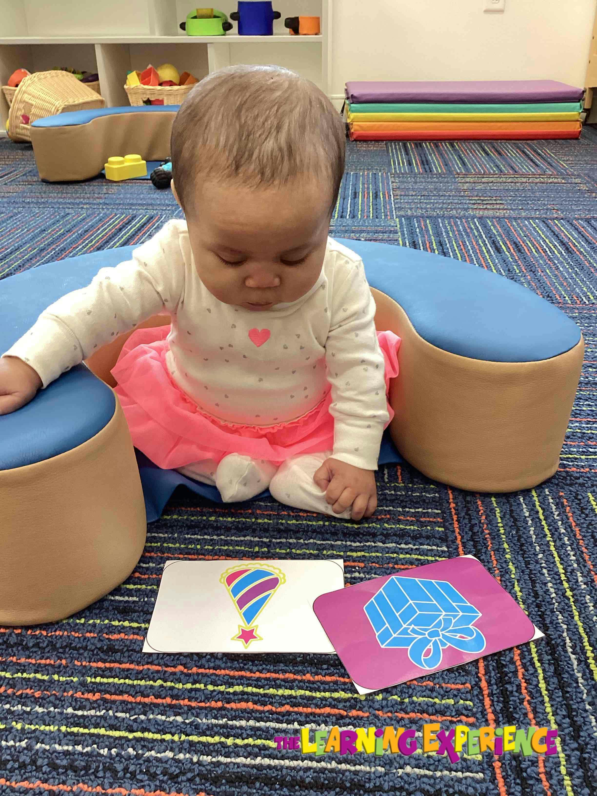 Child sitting on a blue cushion looking at two cards on the floor