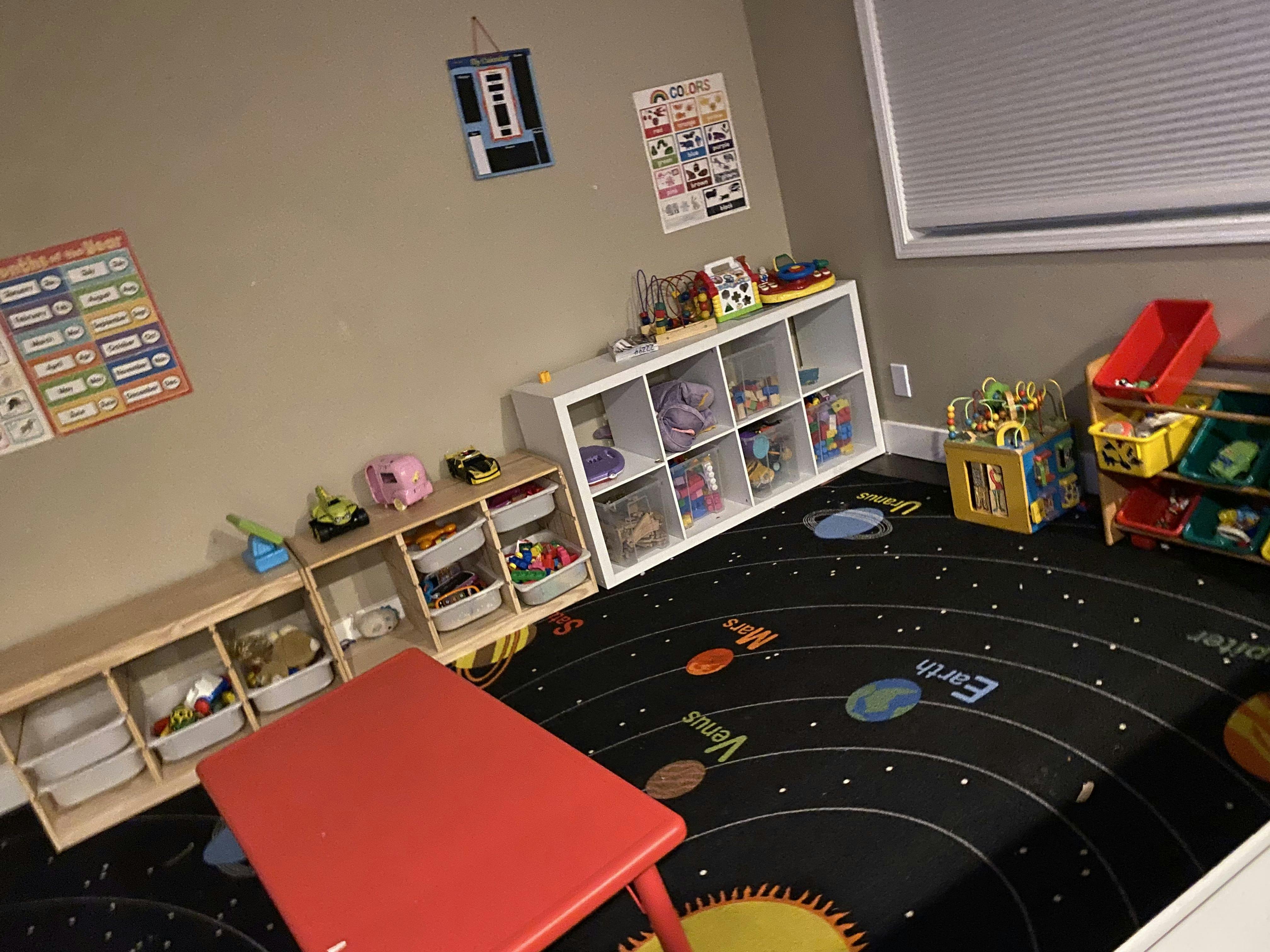 Playroom with toy storage shelves, a red table, and a solar system rug