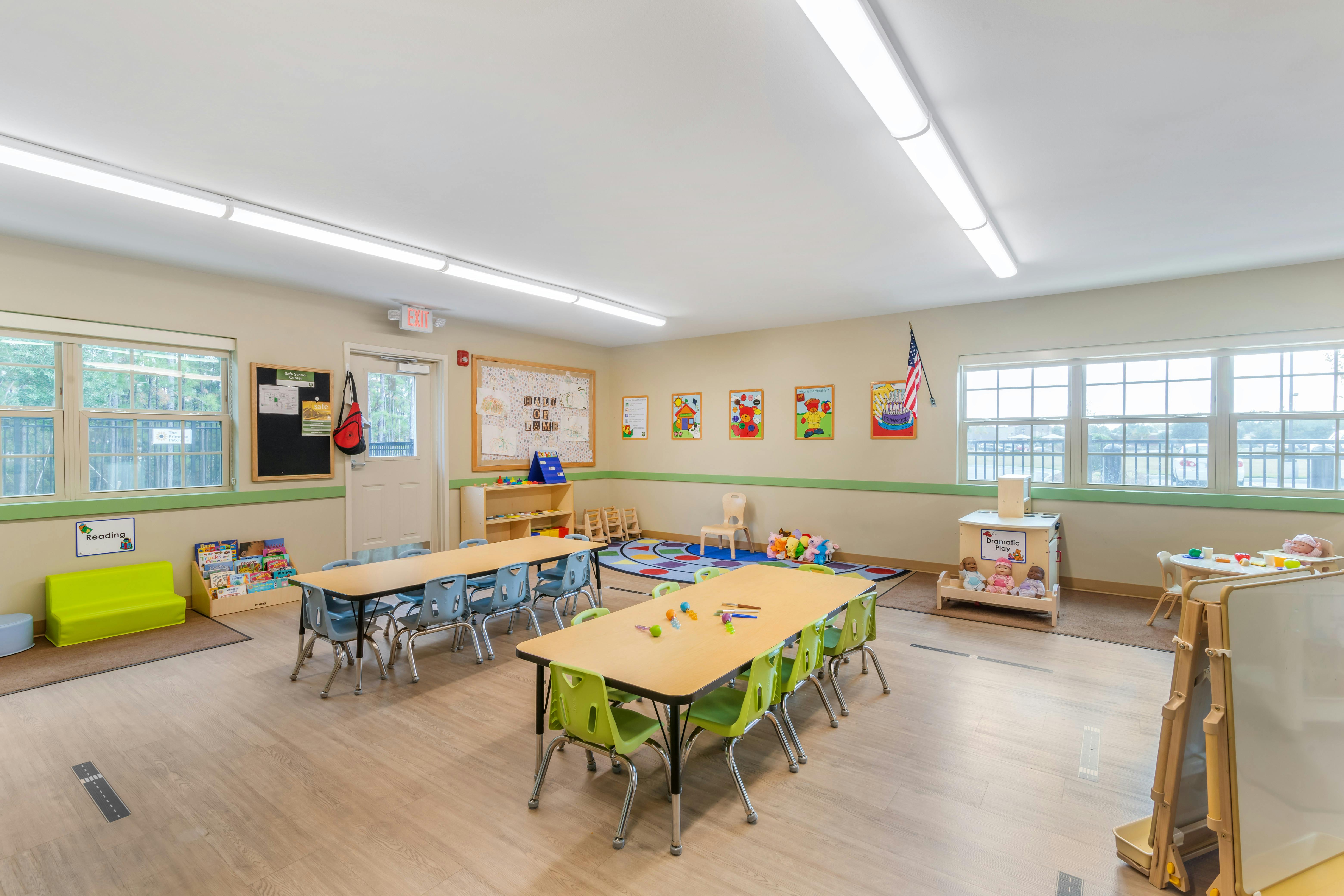 Empty classroom with tables and chairs, a reading corner, and a dramatic play area